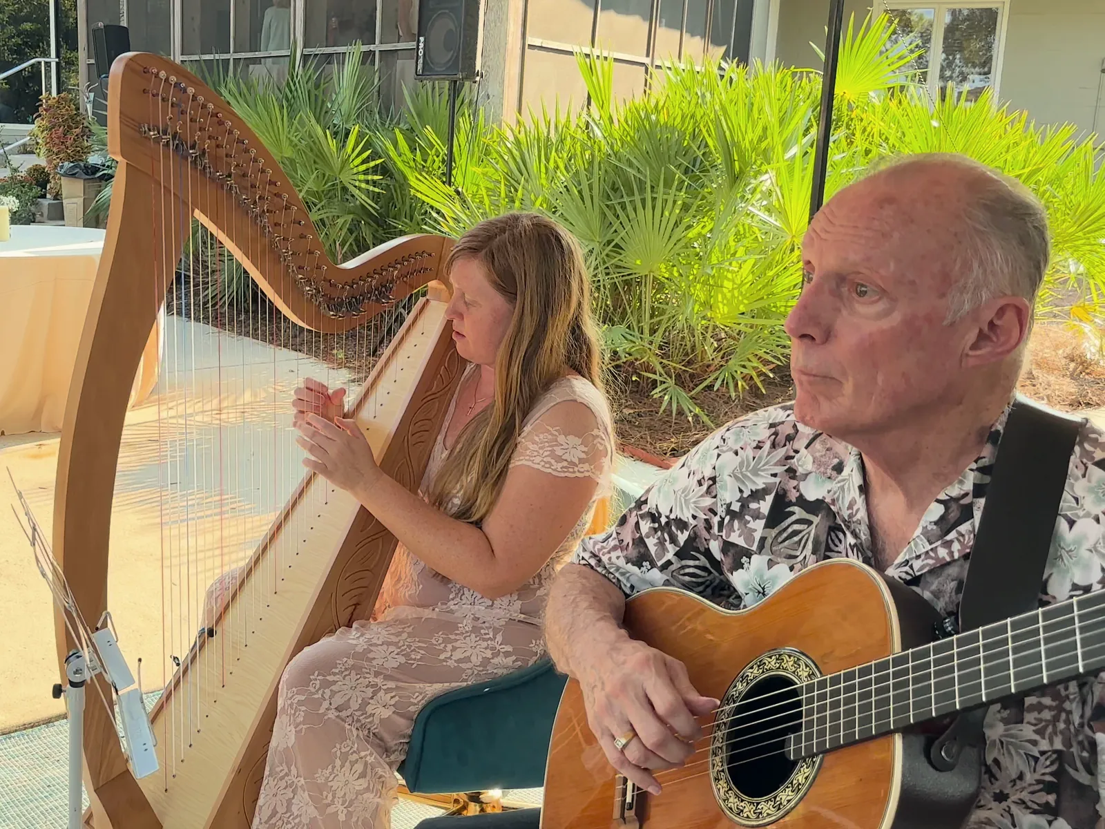 Hilary Turner playing harp beside a guitarist at an outdoor celebration.