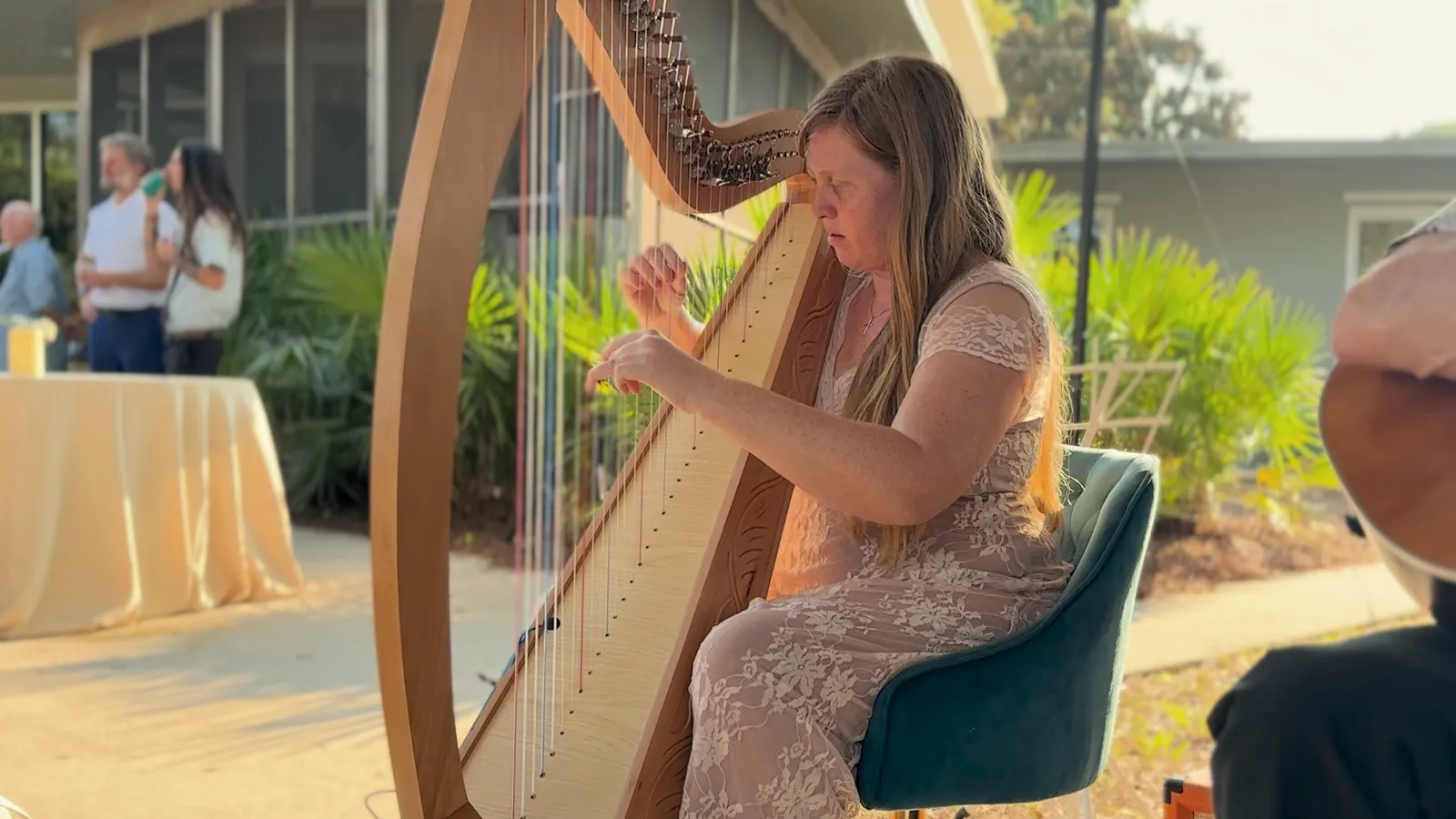 Hilary Turner playing harp at an outdoor celebration in golden-hour light.